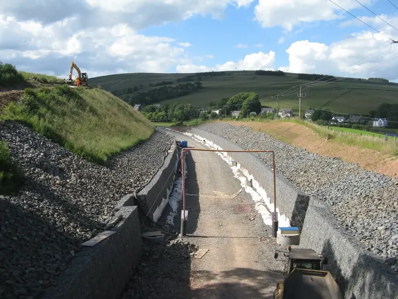 A new track bed in a rail cutting, with retaining walls on both sides and an excavator on the slope