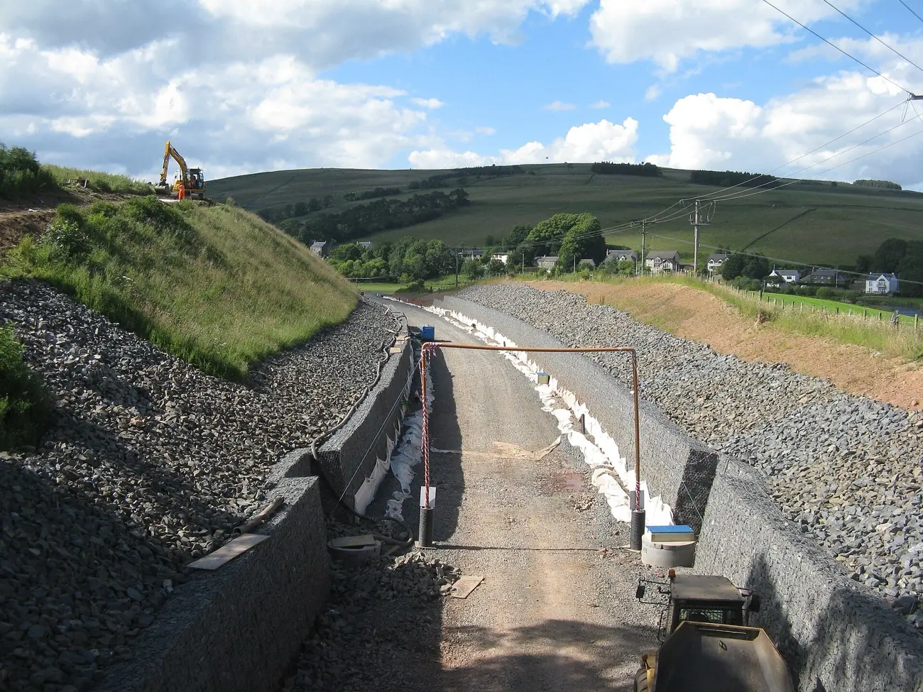 A new track bed in a rail cutting, with retaining walls on both sides and an excavator on the slope